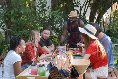 Group of happy friends eating and drinking beers at barbecue dinner camping in nature and having meal together outdoor as summer lifestyle  food and friendship concept