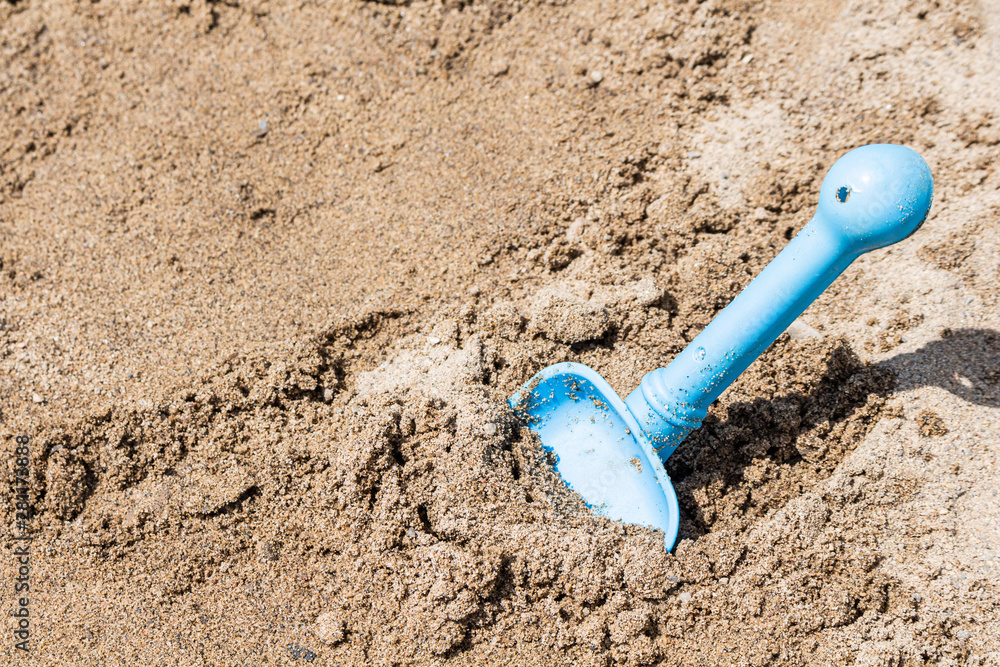 A plastic toy shovel shows off its vibrant blue color, standing up in the sand on a summertime beach. A plastic toy shovel shows off its vibrant blue color, standing up in the sand on a summertime beach.