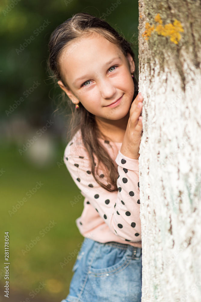 A girl stands behind a tree in the park. Photographed close up. A girl stands behind a tree in the park. Photographed close up.