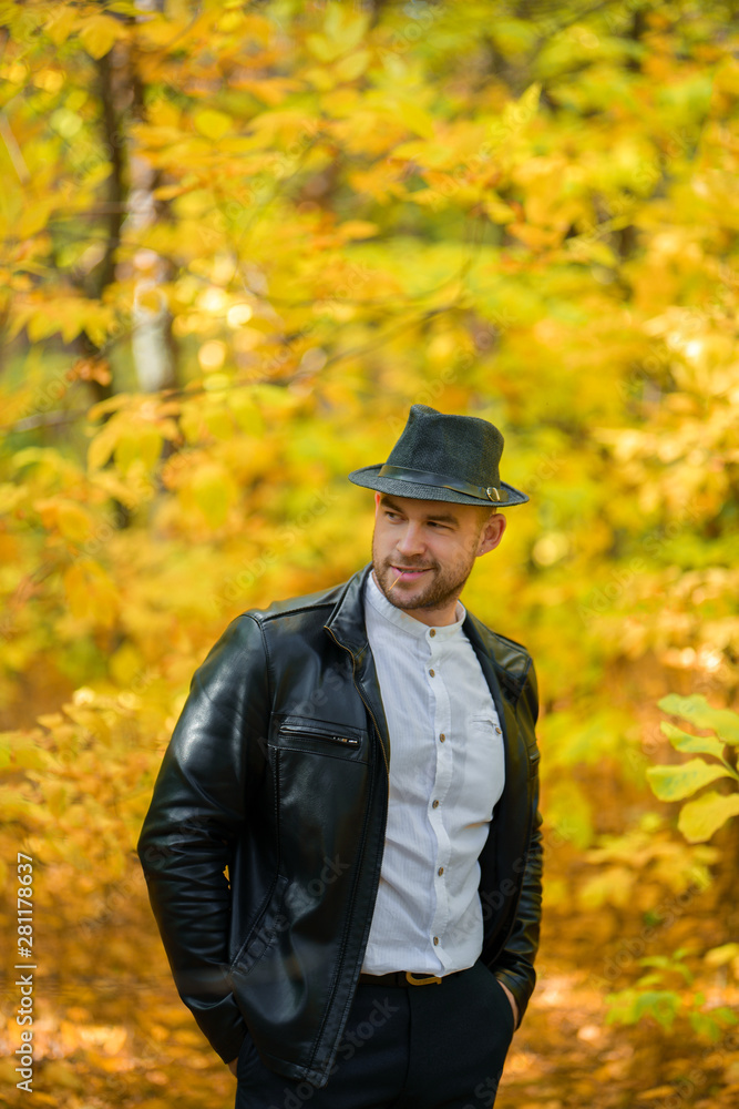 Smiling man in black hat, leather jacket, white shirt and dark trousers on yellow autumn background. Autumn background. Smiling young man. Vertical photography