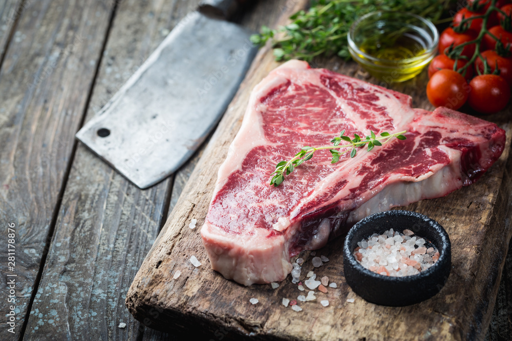 Raw T-bone Steak with fresh herbs and oil on dark wooden background