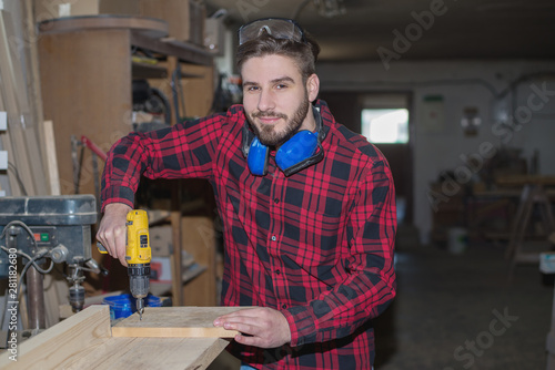 Carpenter working with electric planer on wooden plank in workshop