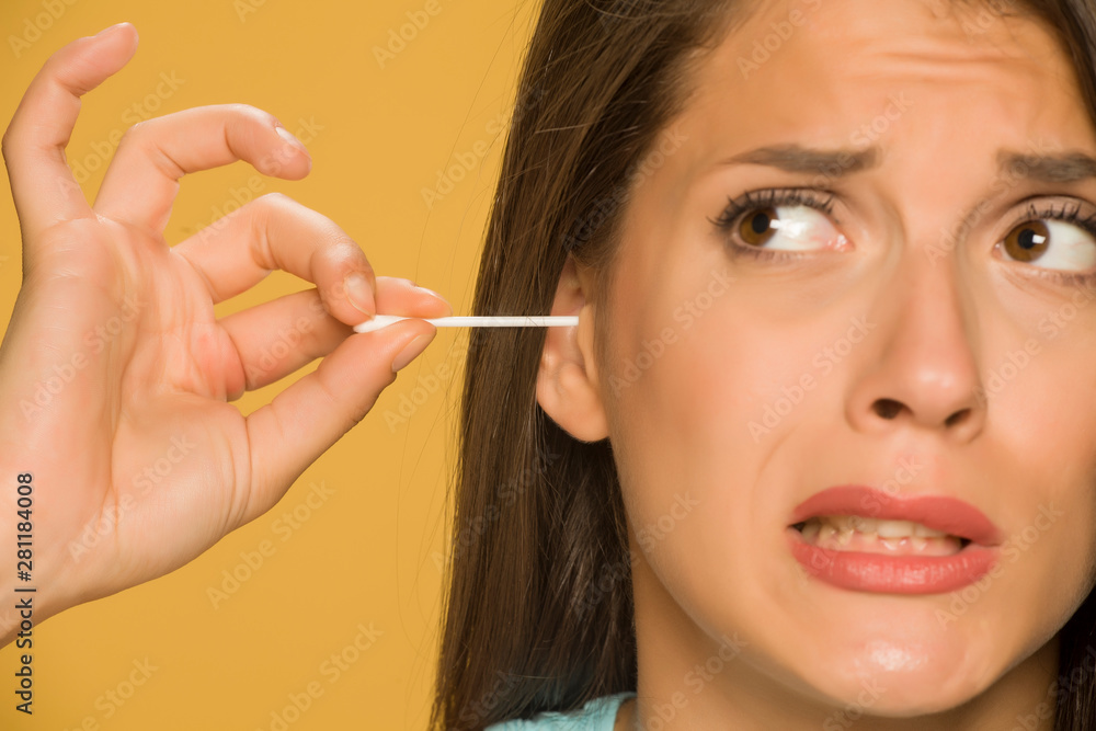 Young woman cleaning her ears with cotton sticks on yellow background Young woman cleaning her ears with cotton sticks on yellow background