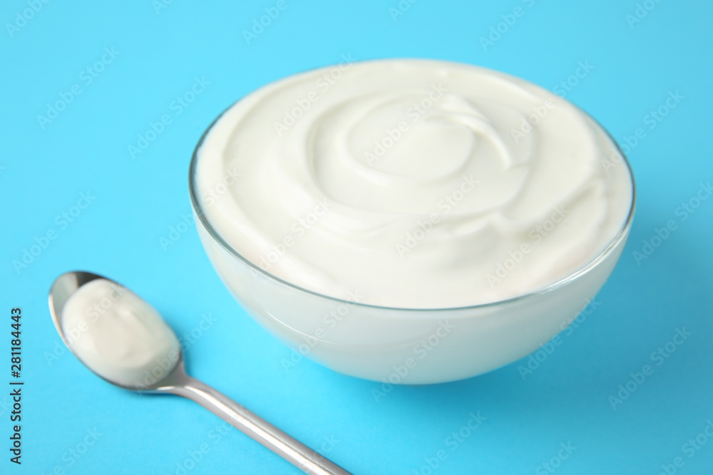 Glass bowl of sour cream and spoon on light blue background Glass bowl of sour cream and spoon on light blue background