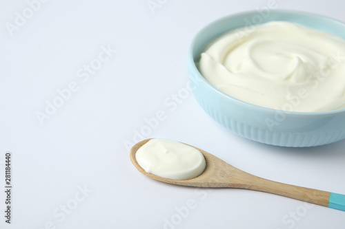 Bowl of sour cream and wooden spoon on white background