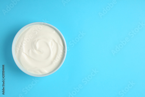 Bowl of sour cream on light blue background, top view. Space for text