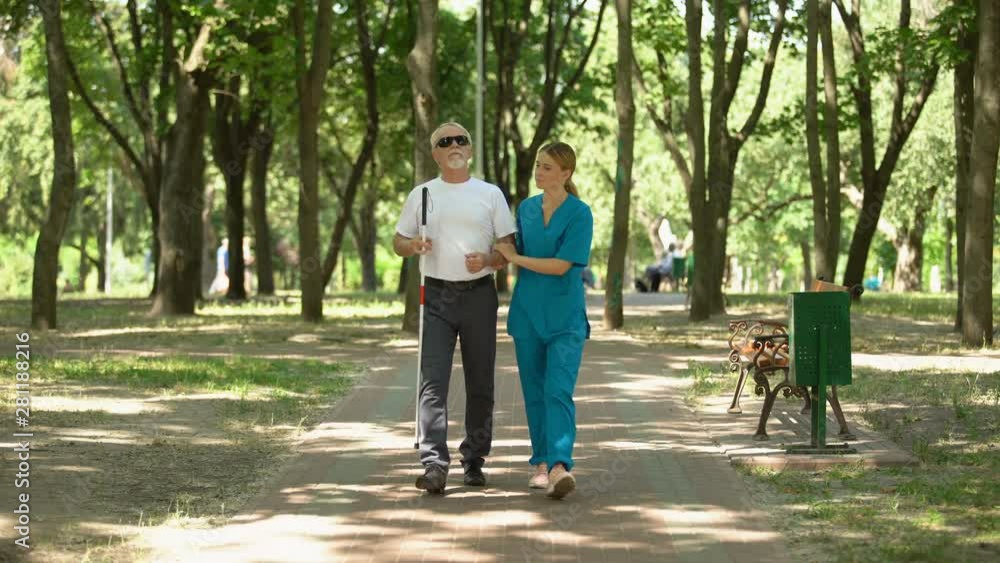 Young nurse holding blind old patient walking in park, vision restore clinic Young nurse holding blind old patient walking in park, vision restore clinic