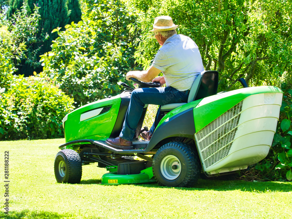 Senior man driving a tractor lawn mower in garden with flowers Senior man driving a tractor lawn mower in garden with flowers