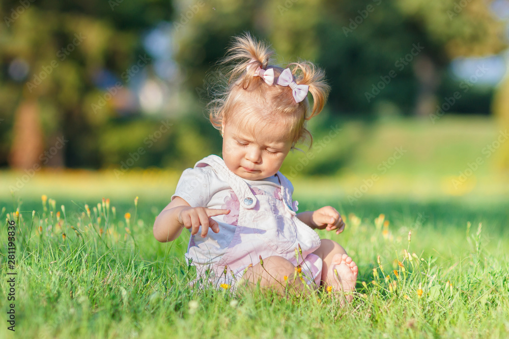 Cute little girl sits on the green grass, outdoors, summer time, blurred background Cute little girl sits on the green grass, outdoors, summer time, blurred background