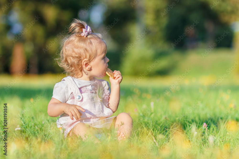 Cute little girl sits on the green grass, outdoors, summer time, blurred background Cute little girl sits on the green grass, outdoors, summer time, blurred background