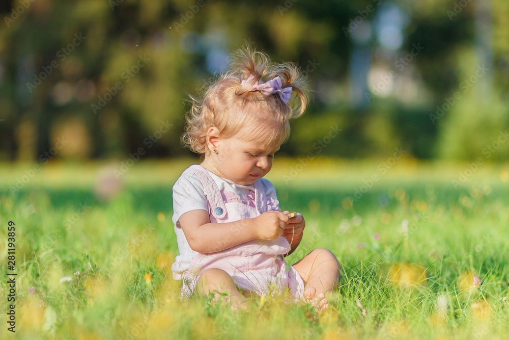 Cute little girl sits on the green grass, outdoors, summer time, blurred background Cute little girl sits on the green grass, outdoors, summer time, blurred background