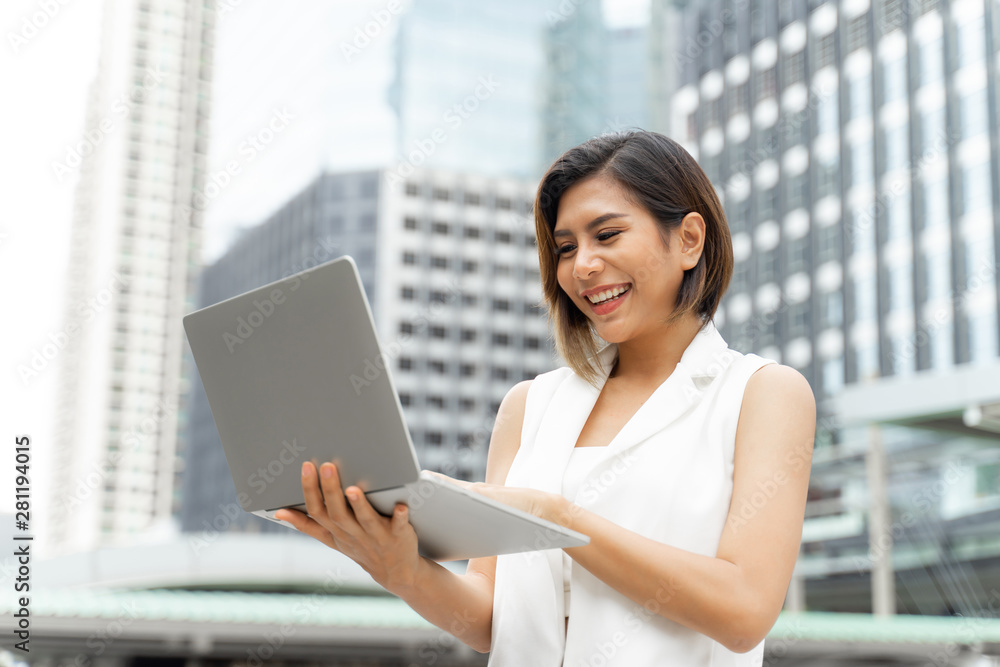 Beautiful Asian cute girl smiling in business woman clothes  using laptop computer  , urban city background