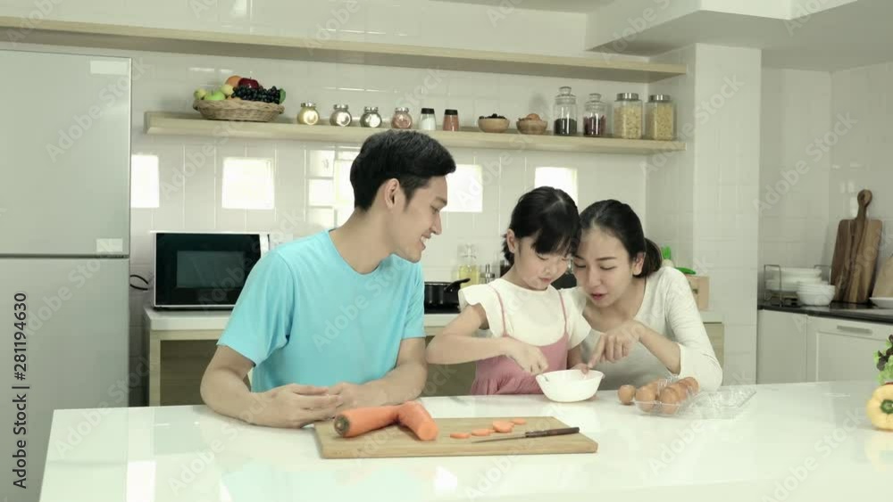 Chinese little girl learning cooking with father and mother in kitchen at home together. Little girl cutting carrot on the table. Concept of family, cooking and food. Chinese little girl learning cooking with father and mother in kitchen at home together. Little girl cutting carrot on the table. Concept of family, cooking and food.