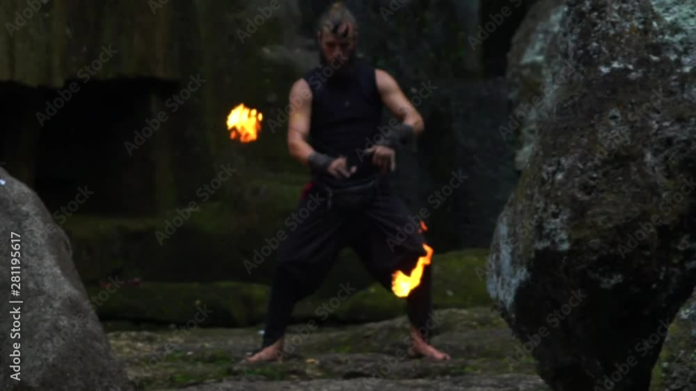 A man with fire in his hands on the background of stones and a waterfall. A man with fire in his hands on the background of stones and a waterfall.