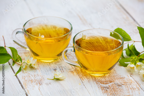 Two cups of green tea with jasmine flowers on grunge wooden table