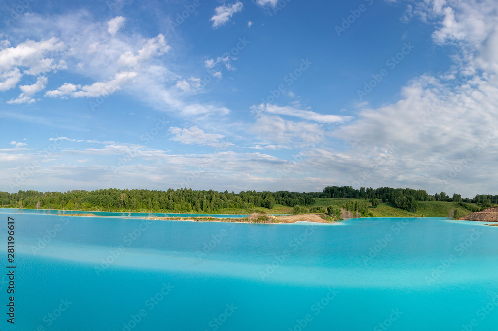 Panorama of a beautiful lake with azure-blue water. Green trees, blue sky with white clouds. Summer sunny day