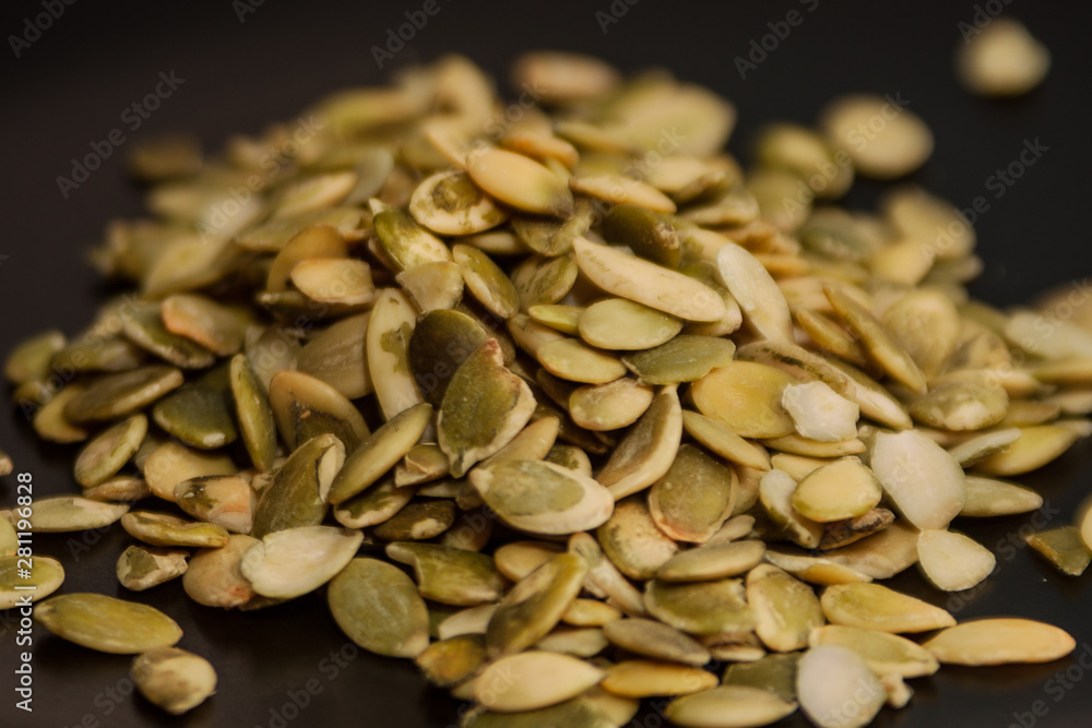 Obraz premium peeled pumpkin seeds on a black background. food closeup. vegan, vegetarian diet, raw foods. eco-friendly diet