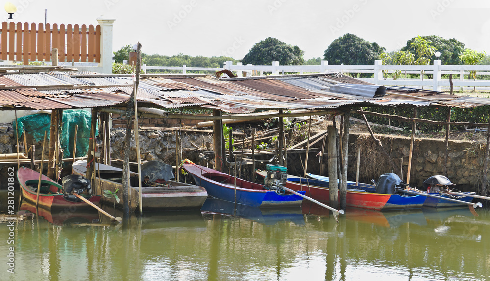 Small fisherman long tailed motor boats docked under old zinc plate roofs in the river avoiding sunlight