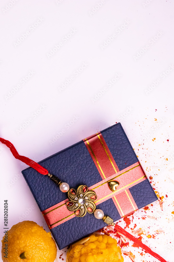 Φωτογραφία Indian festival – Top view of sweets, elegant Rakhi on blue gift box with spread rice, kumkum and haldi haldi on white background