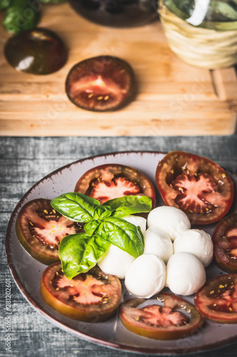 Close up of Italian caprese salad served in plate with basil leaves on rustic table