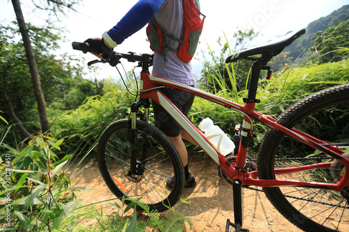 Cross country biking woman cyclist walking with mountain bike on tropical forest trail
