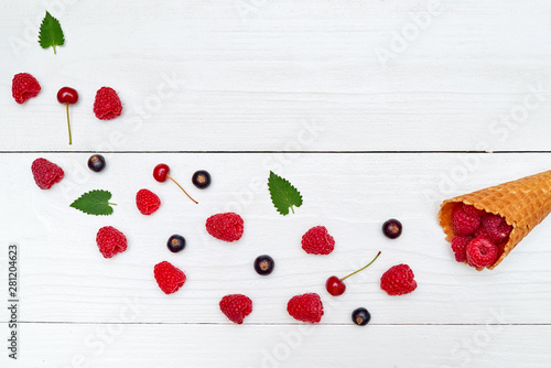 Ripe sweet raspberries, cherries and black currant in ice cream waffle cones; copy space. Fresh berries on white wood background. Summer and healthy food concept. Top view; flat lay