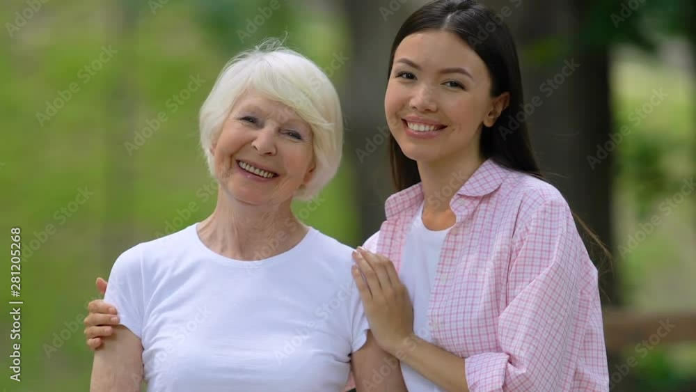 Young woman with elderly grandmother smiling at camera, relaxing outdoors Young woman with elderly grandmother smiling at camera, relaxing outdoors