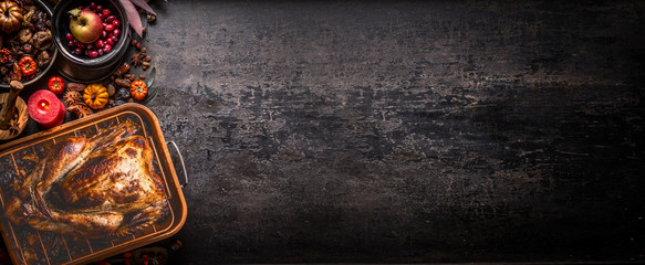 Thanksgiving background with roasted stuffed turkey on dark rustic table with autumn ingredients, pumpkins, candles and nuts and decoration. Top view. Banner. Copy space for your design