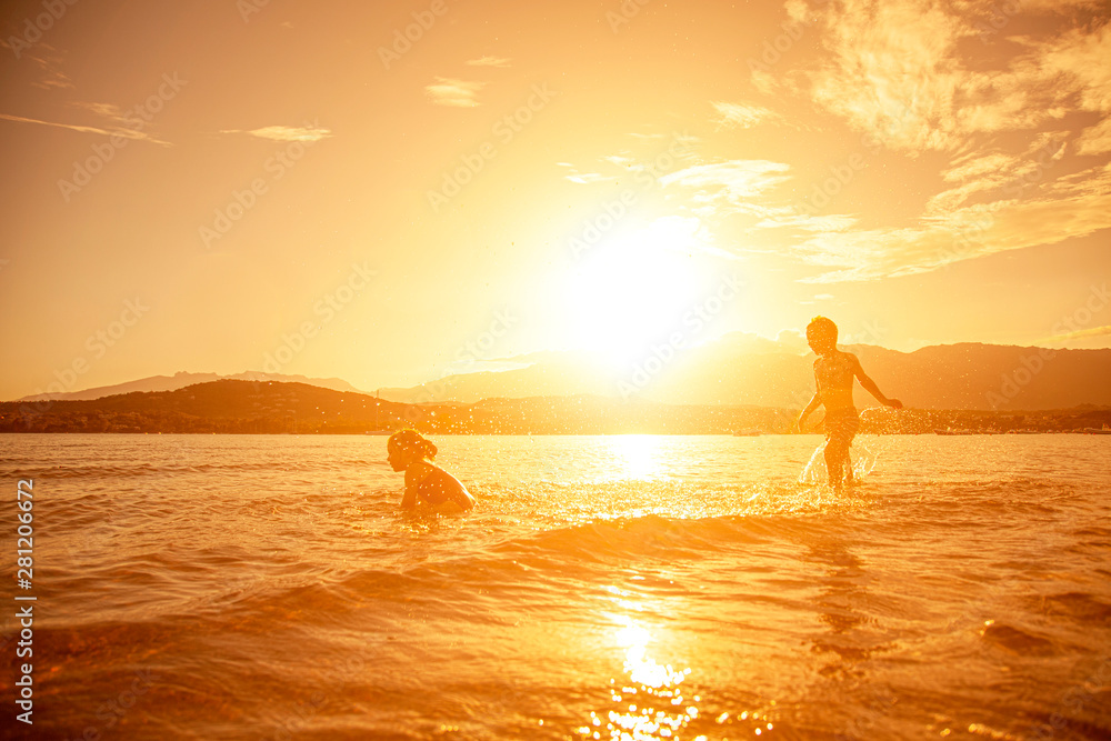pair of children playing in the sea, shot taken at sunset pair of children playing in the sea, shot taken at sunset
