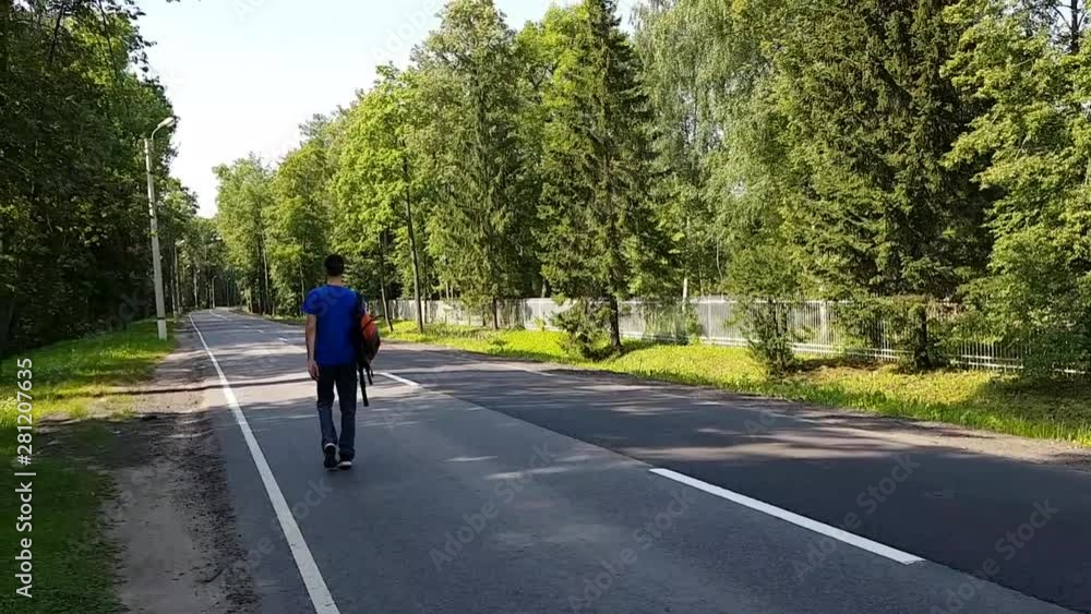 A young man with a limp walks along the road. With a backpack on his shoulders . Travelling alone adult A young man with a limp walks along the road. With a backpack on his shoulders . Travelling alone adult