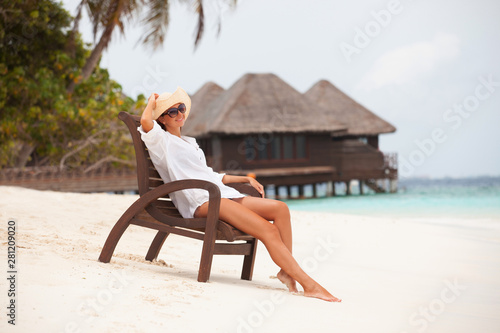 Young tanned woman sit at the chair and relax near bungalow of resort on the beach. Happy woman vacation. Island lifestyle. Rest on the beach at summertime © Dmytro Sunagatov