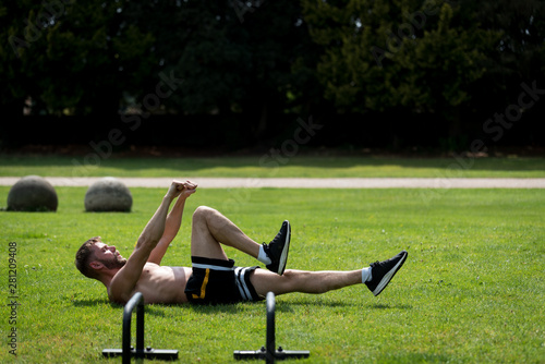 Man performing warm up before doing calisthenics fitness workout in an outdoor public park, UK