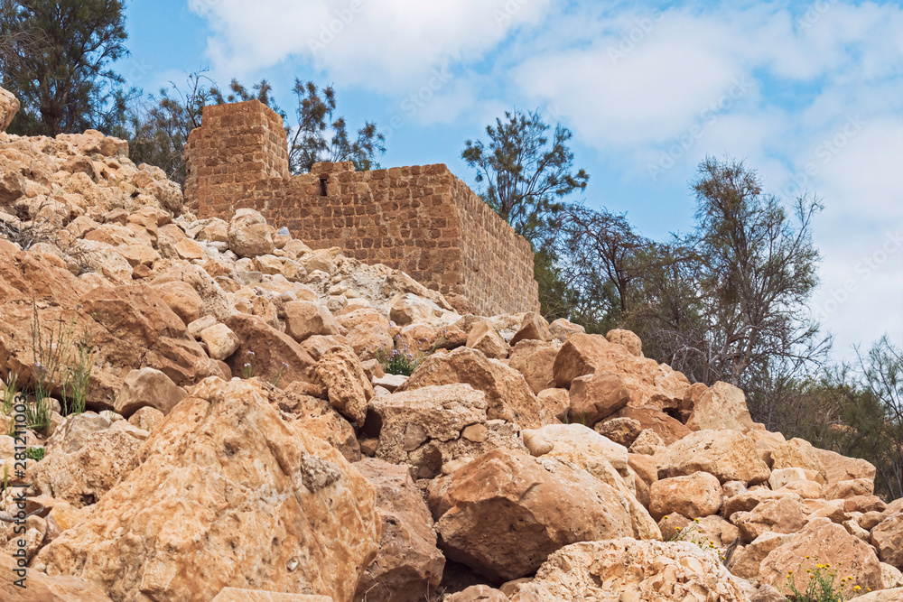 low angle view of the stone mamluk era flour mill at ein gedi spring in israel with a rocky hillside in the foreground and cloudy sky in the background
