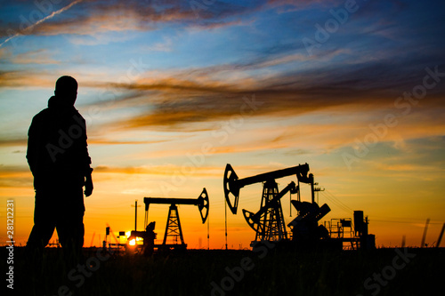 Silhouette of the worker on the background of oil rockers. Sunset. Oil production in Russia.