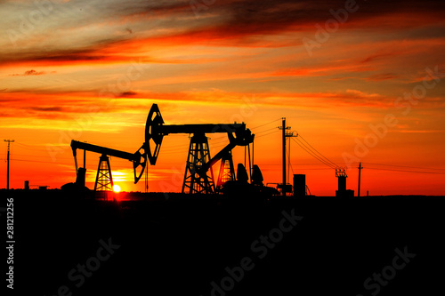 Pumping unit is working in oil field of the sunset. The contours of the oil rocking on the background of a beautiful sunset.