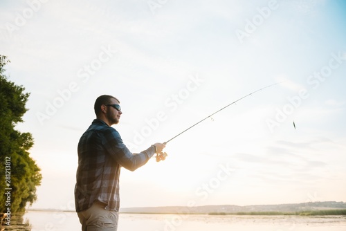 Fisher man fishing with spinning rod on a river bank at misty foggy sunrise. fisher with spinning. spinning concept