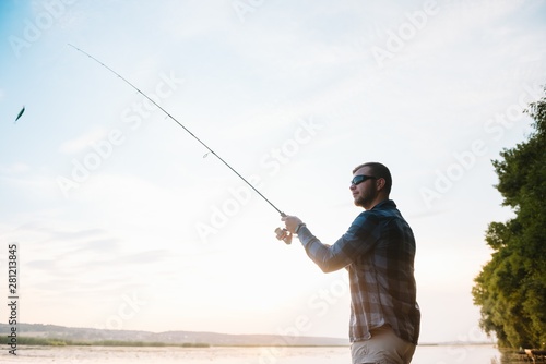 Fisher man fishing with spinning rod on a river bank at misty foggy sunrise. fisher with spinning. spinning concept