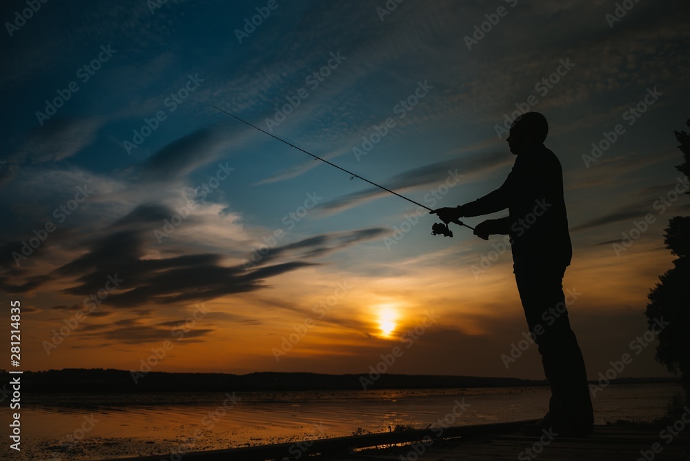 Fisherman at sunset on the river .Beautiful summer landscape with sunset on the river. Fishing. spinning at sunset. Silhouette of a fisherman
