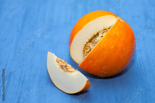 Yellow honey melon half with the seeds and slice on a blue wooden background. Juicy fruit.