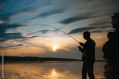 Fisherman at sunset on the river .Beautiful summer landscape with sunset on the river. Fishing. spinning at sunset. Silhouette of a fisherman