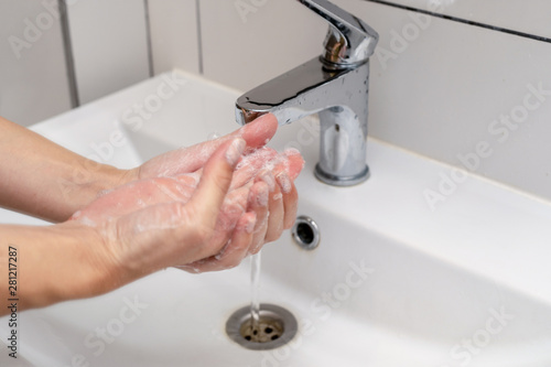Women washing hands in the bathroom in the sink using purple color soap. Foam on hands