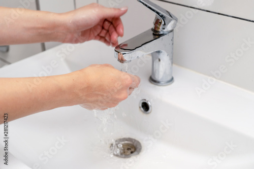 Women finish washing hands in the bathroom in the sink using purple color soap. Female hands under the tap and the water jet