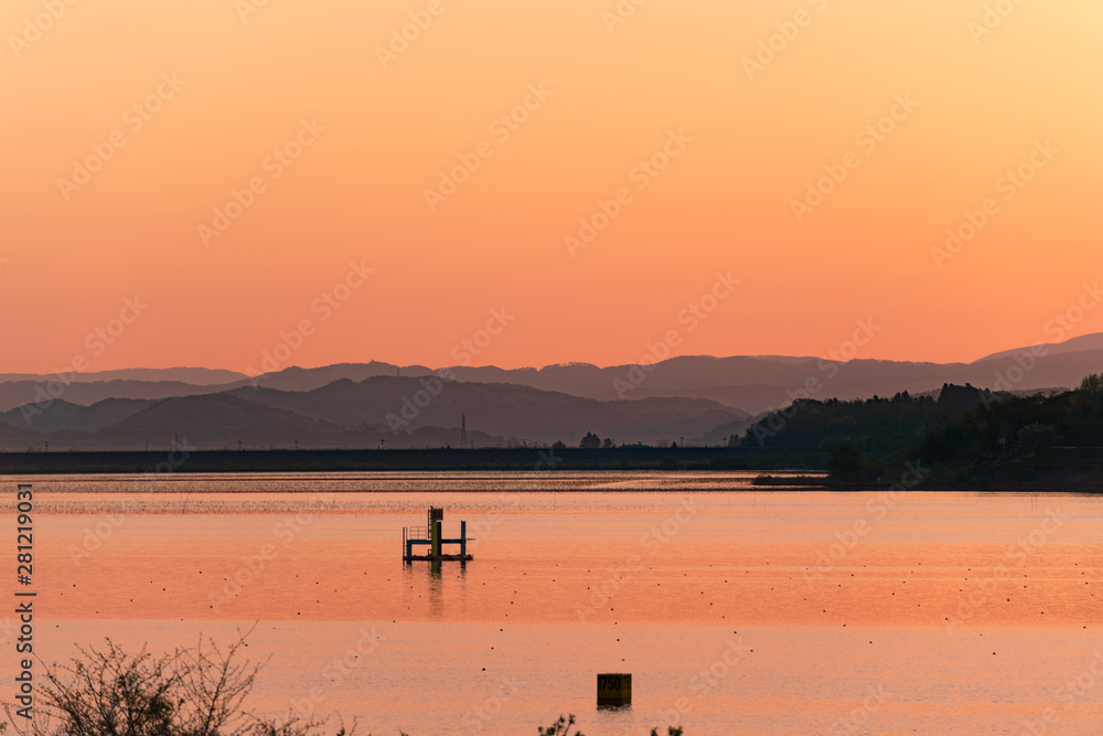 夜明けで朝もやに赤く染まる長沼湖面