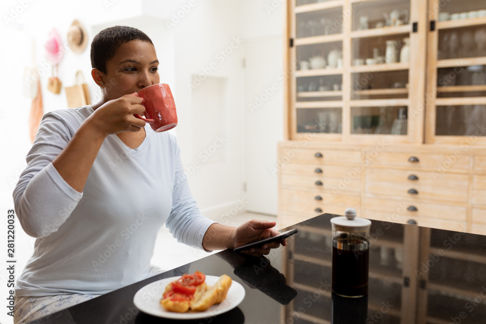 Woman using mobile phone while having coffee on a dining table