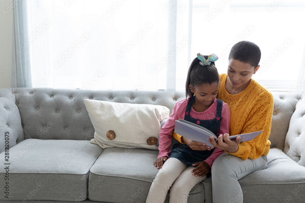 Mother and daughter reading a story book on a sofa in living room Mother and daughter reading a story book on a sofa in living room