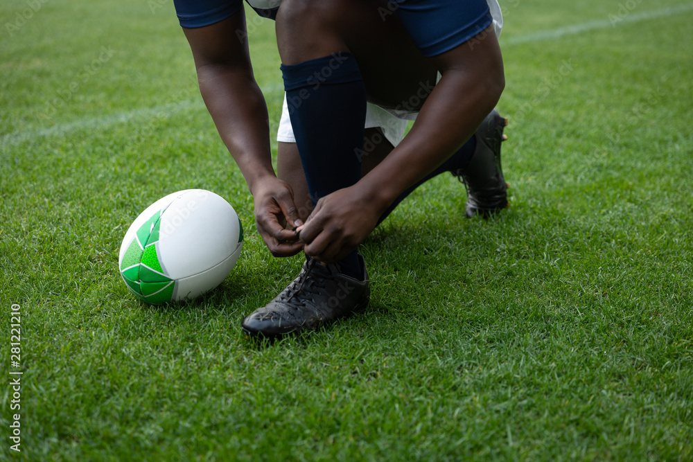 African american male rugby player tying shoelaces in the stadium African american male rugby player tying shoelaces in the stadium