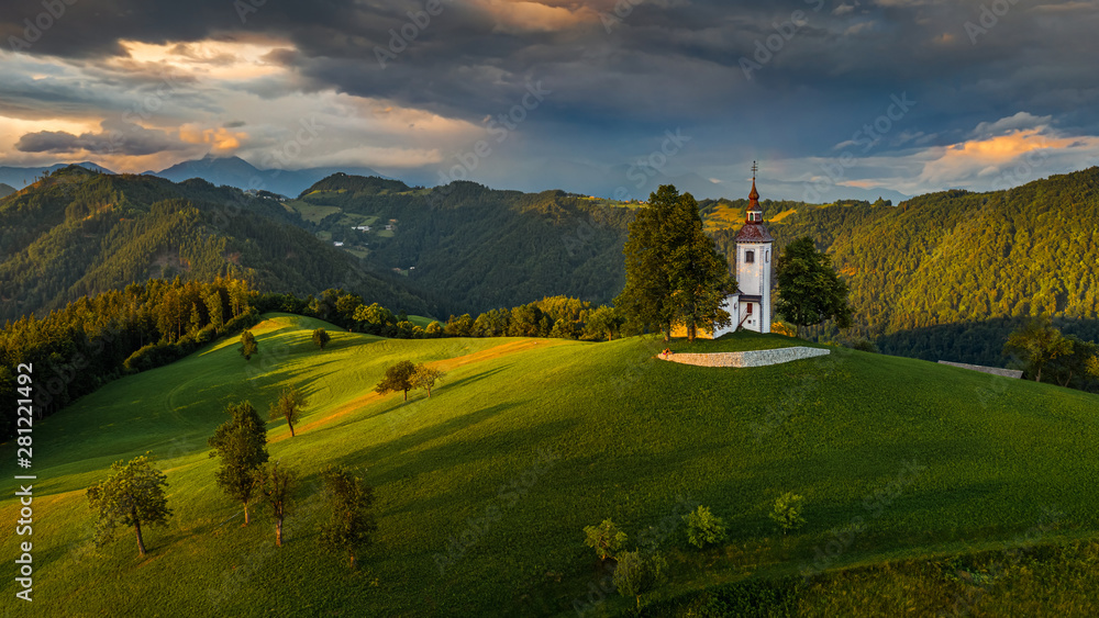 Skofja Loka, Slovenia - Aerial view of the beautiful hilltop church of Sveti Tomaz (Saint Thomas) with an amazing colorful sunset and the Julian Alps at background at summer time
