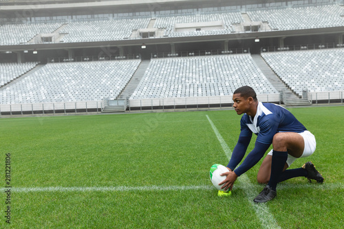African American male rugby player placing rugby ball on a stand in stadium
