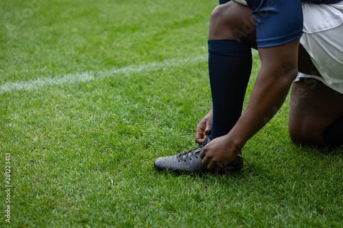  African american Male rugby player tying shoelaces in the stadium