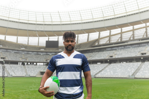 African American rugby player standing with rugby ball in stadium